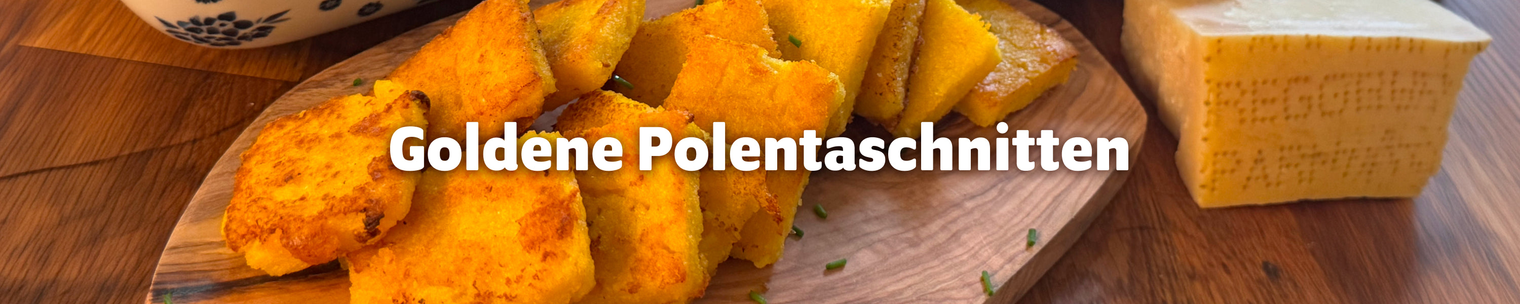 Goldbraun angebratene Polentaschnitten auf einem Holzbrett angerichtet, daneben ein Stück Parmesan – Rezept für glutenfreie Polentaschnitten