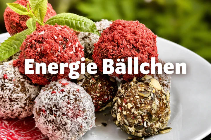 Bunte Energiebällchen mit Erdbeer-, Kokos- und Kürbiskern-Panade auf weißem Teller, Schriftzug „Energie Bällchen"