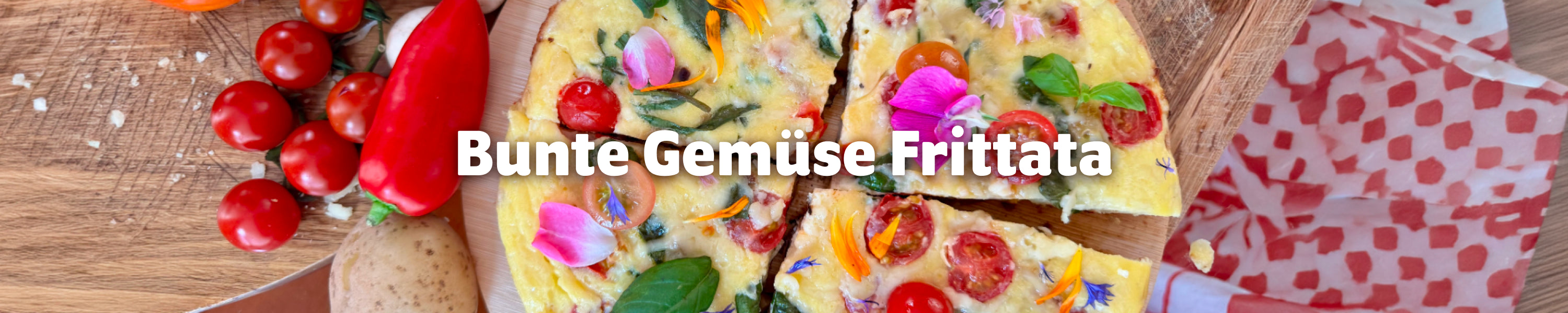 Nahaufnahme einer aufgeschnittenen Gemüse-Frittata mit Cherrytomaten, Basilikum und bunten essbaren Blüten.