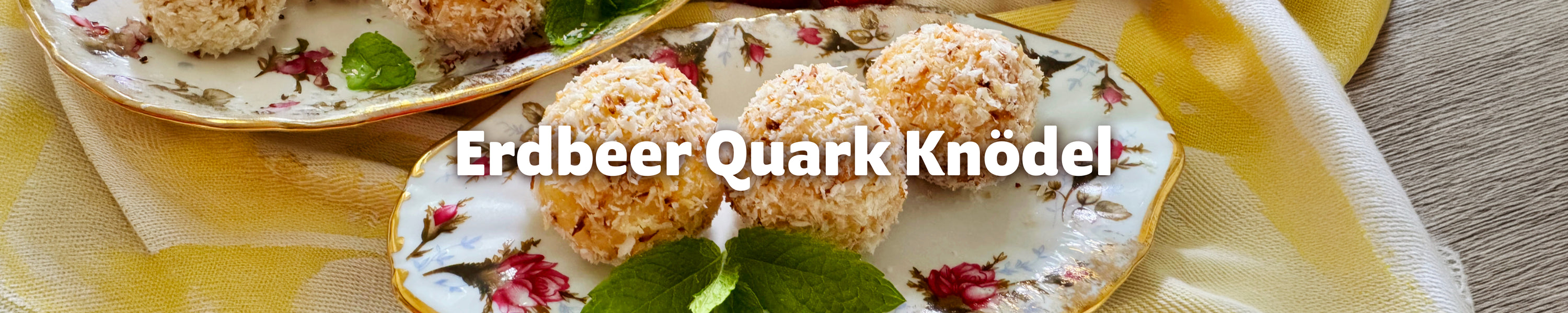 Hausgemachte Erdbeer-Quark-Knödel mit Kokosraspeln auf einem floralen Teller, dekoriert mit frischer Minze und Erdbeeren.