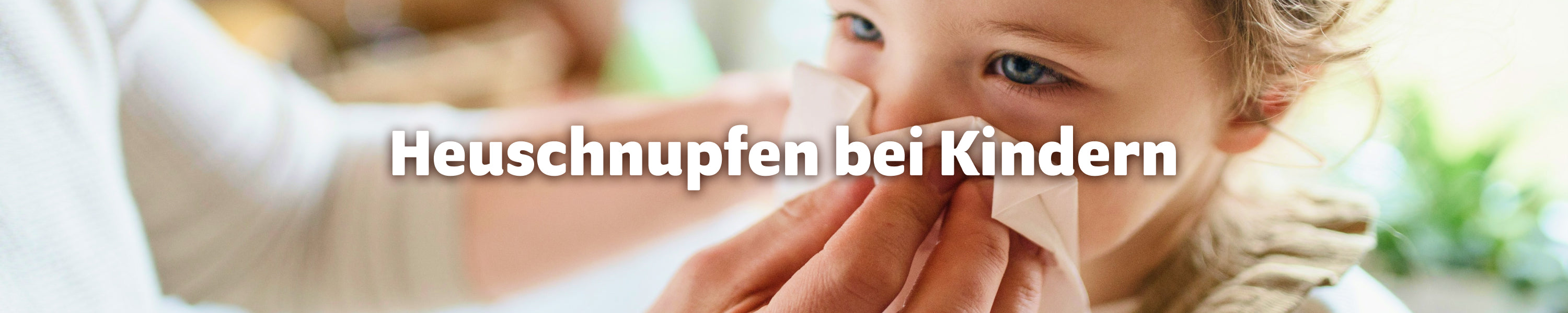 Heuschnupfen bei Kindern: Elternteil wischt die laufende Nase eines Kindes mit einem Taschentuch ab.